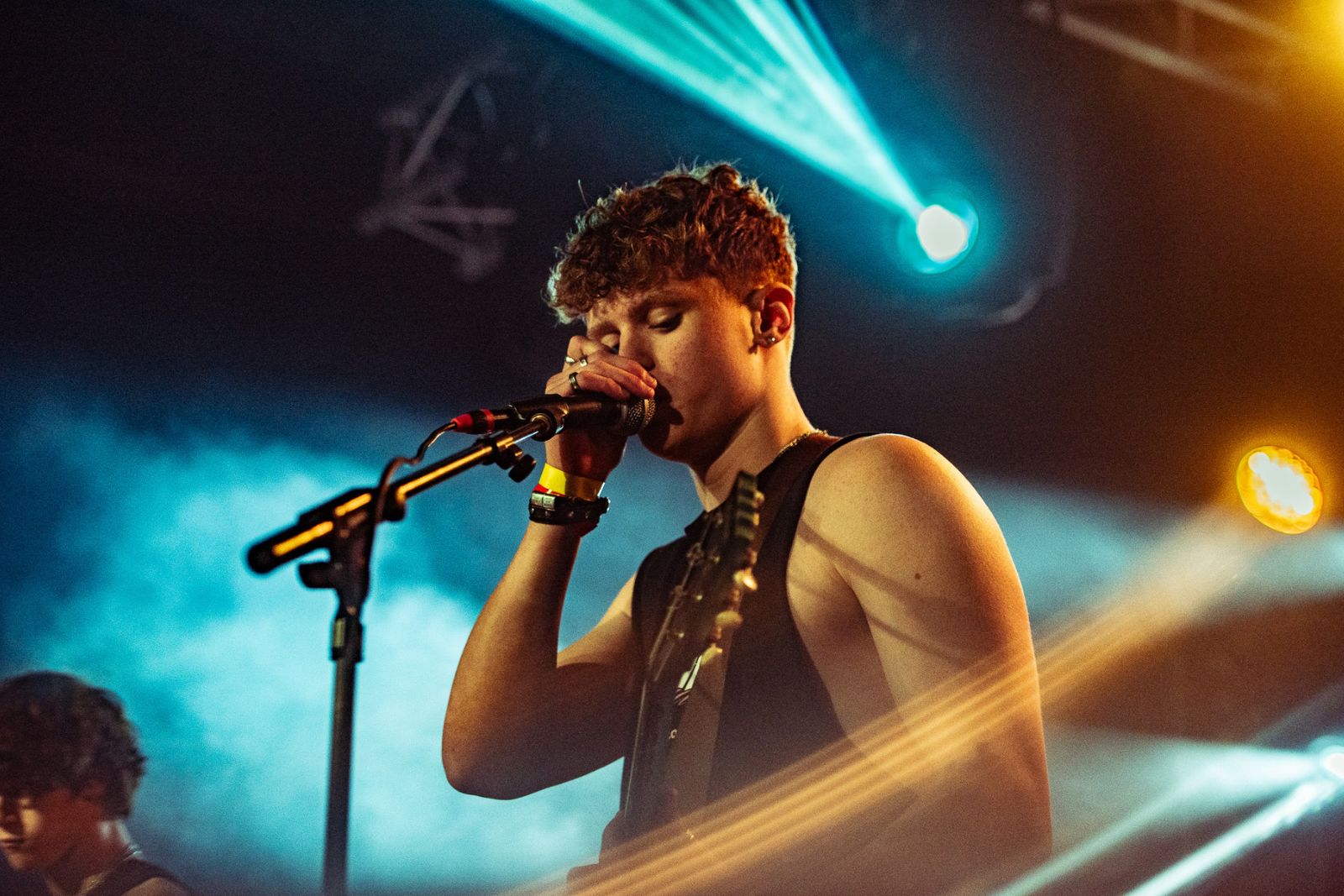 Norwich performer on stage, singing into microphone with guitar